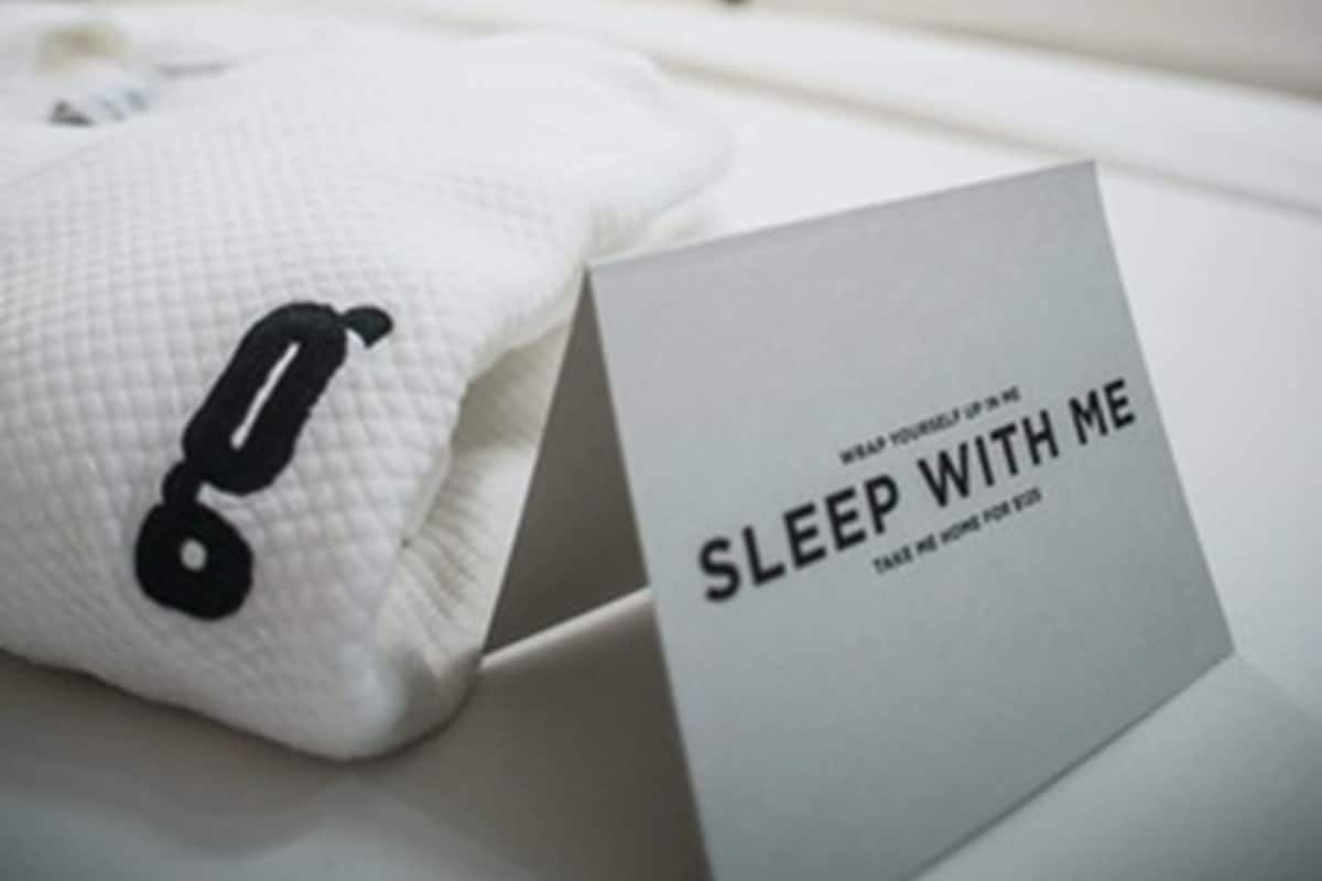 A neatly made bed with a pillow and a sign that reads "SLEEP WITH ME".