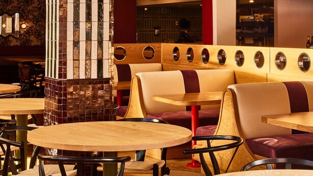 A restaurant interior with wooden tables and booths, a tiled pillar, and a unique ceiling design.