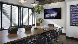 A conference room with a long table, chairs, a potted plant, a tablet, and a TV on the wall.