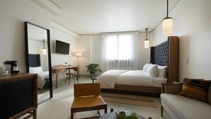 A hotel room with a bed, a desk, a chair, a sofa, a TV, and a large mirror.