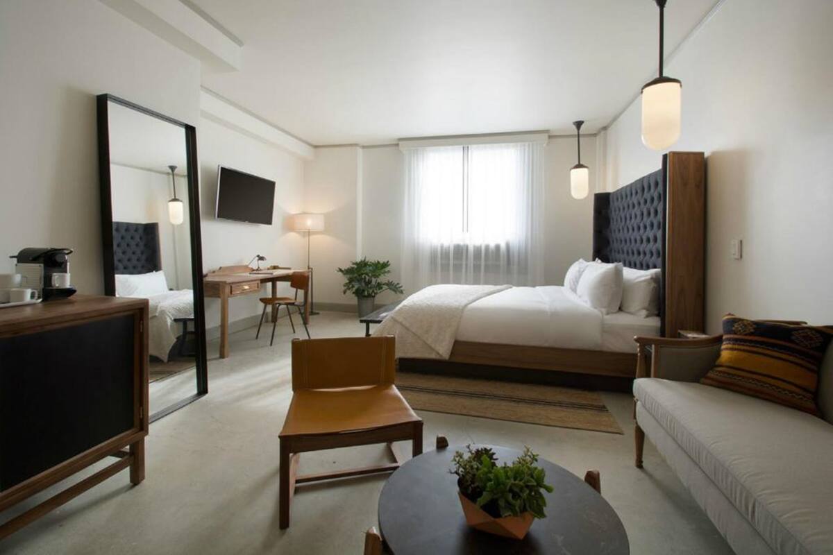 A hotel room with a bed, a desk, a chair, a sofa, a TV, and a large mirror.