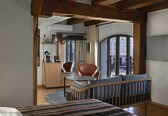 A cozy room with a wooden crib, a dining table with chairs, a kitchen area, and a large window offering a city view.