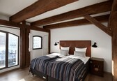A bedroom with a large bed, wooden beams, a city view, and a small bedside table.