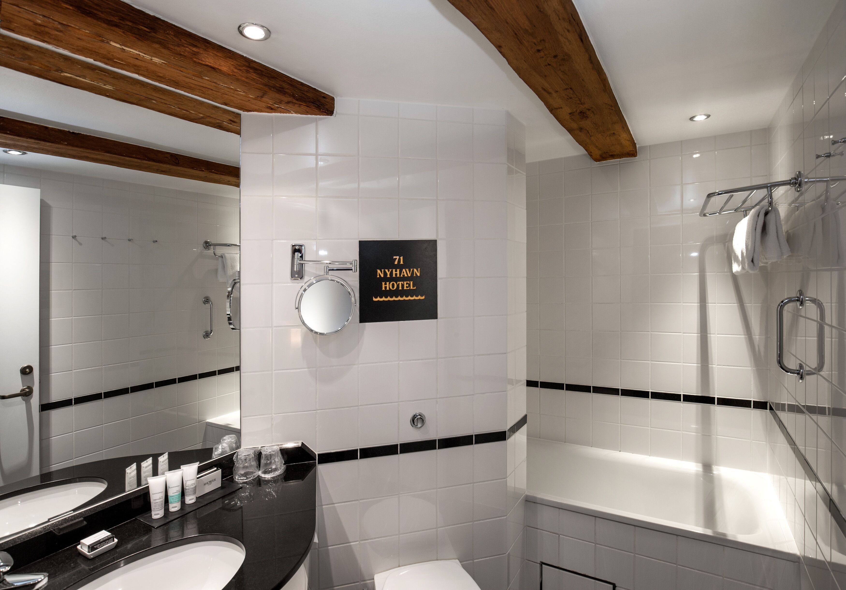 A modern bathroom with a double sink, a bathtub, and a shower. A sign indicates the location as 71 Nyhavn Hotel.