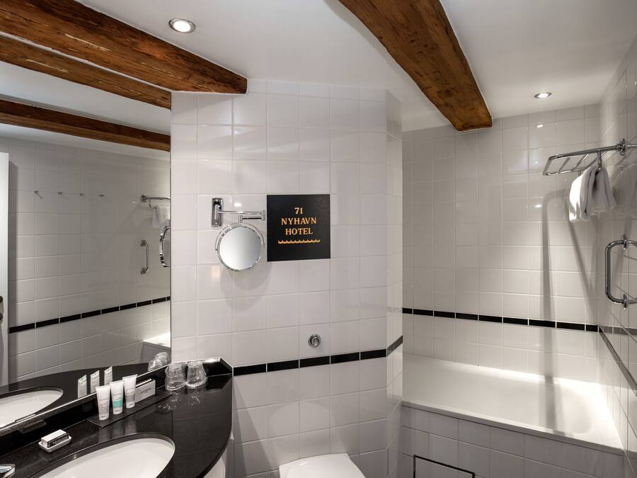 A modern bathroom with a double sink, a bathtub, and a shower. A sign indicates the location as 71 Nyhavn Hotel.
