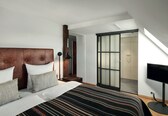 A bedroom with a large bed, a wooden headboard, a TV, and a sliding glass door leading to a bathroom.