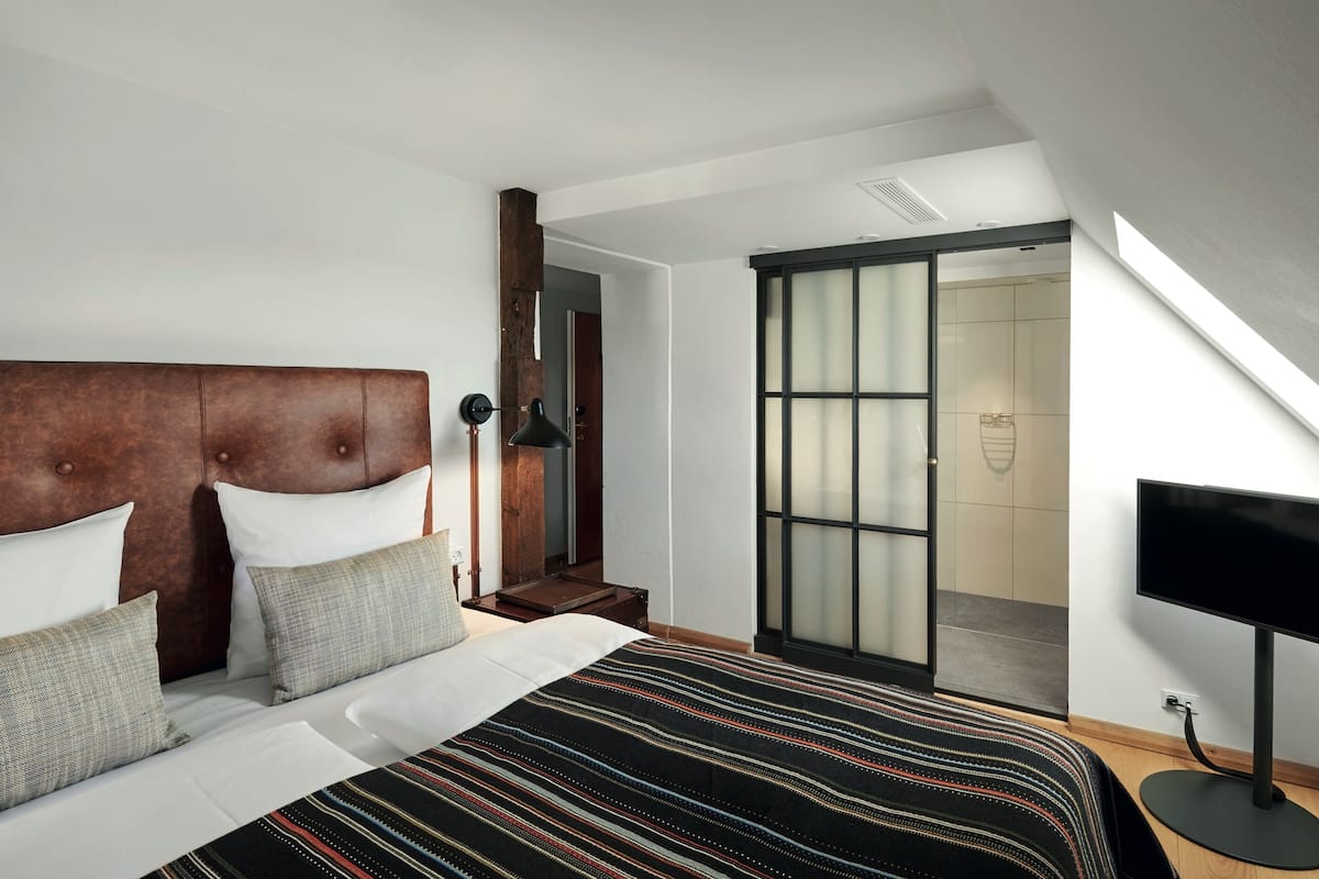 Une chambre à coucher avec un grand lit, une tête de lit en bois, une télévision et une porte-fenêtre coulissante donnant sur une salle de bain.