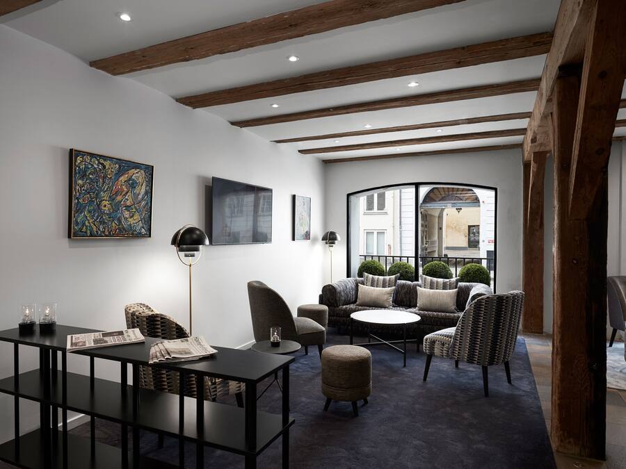 A modern living room with a dark carpet, wooden beams, a round coffee table, and a sofa with multiple cushions.