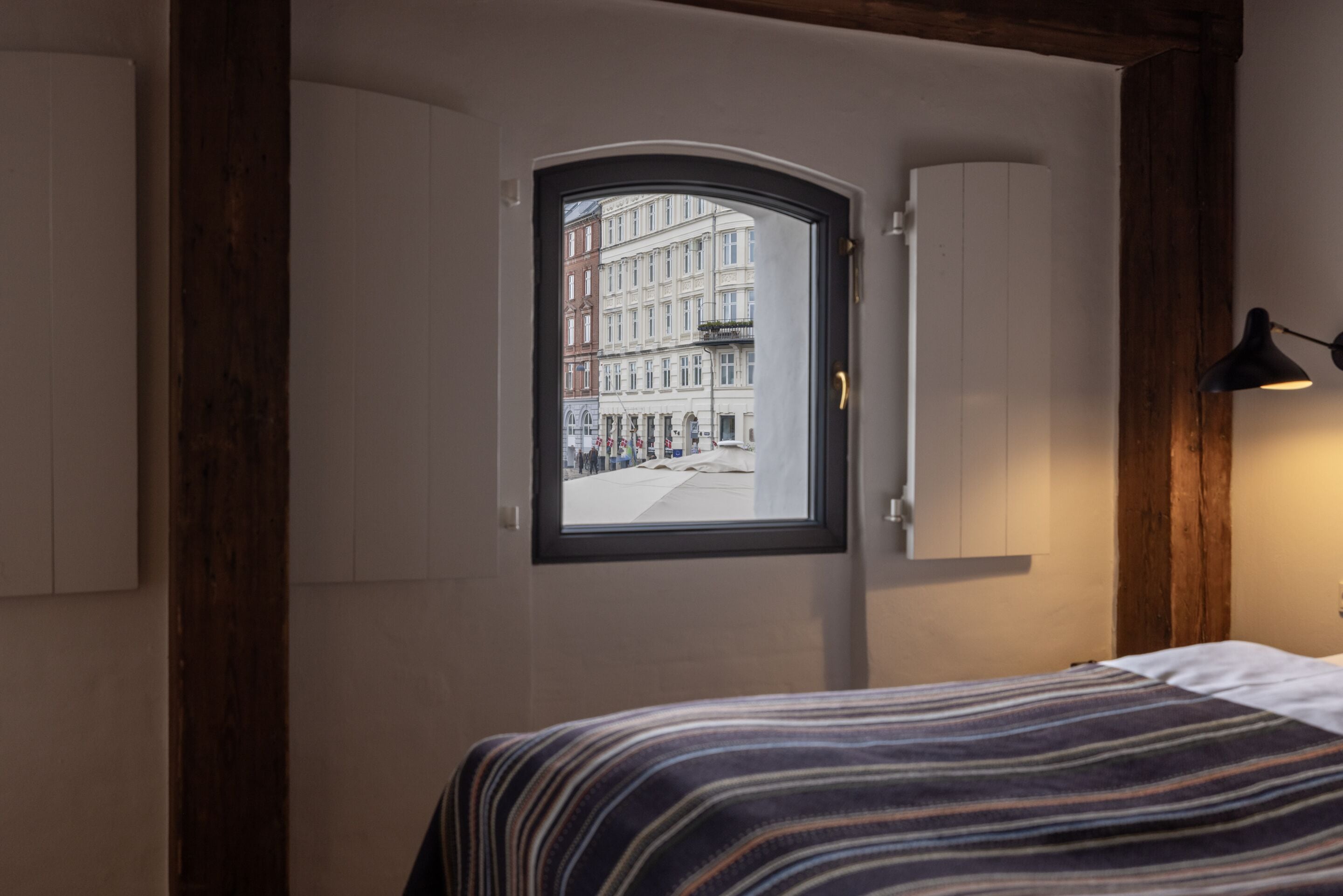 Un dormitorio con vista a una calle de la ciudad, una cama con colcha a rayas y techo de madera.