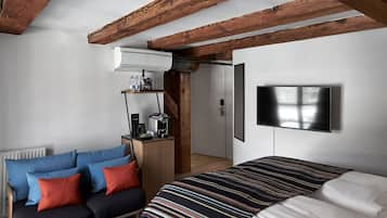 A bedroom with a bed, a sofa, a TV mounted on the wall, and a wooden ceiling.