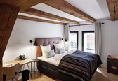 A bedroom with a bed, bedside table, lamp, and a view of the outside.