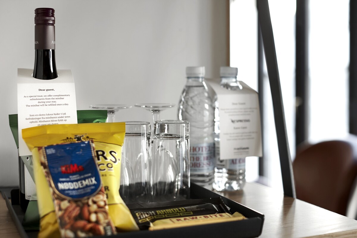 A tray with a bottle of wine, glasses, a water bottle, a bag of nuts, and a chocolate bar.