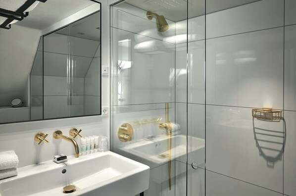 A modern bathroom with a white sink, gold fixtures, and a glass-enclosed shower area. - 71 Nyhavn Hotel (Copenhagen)