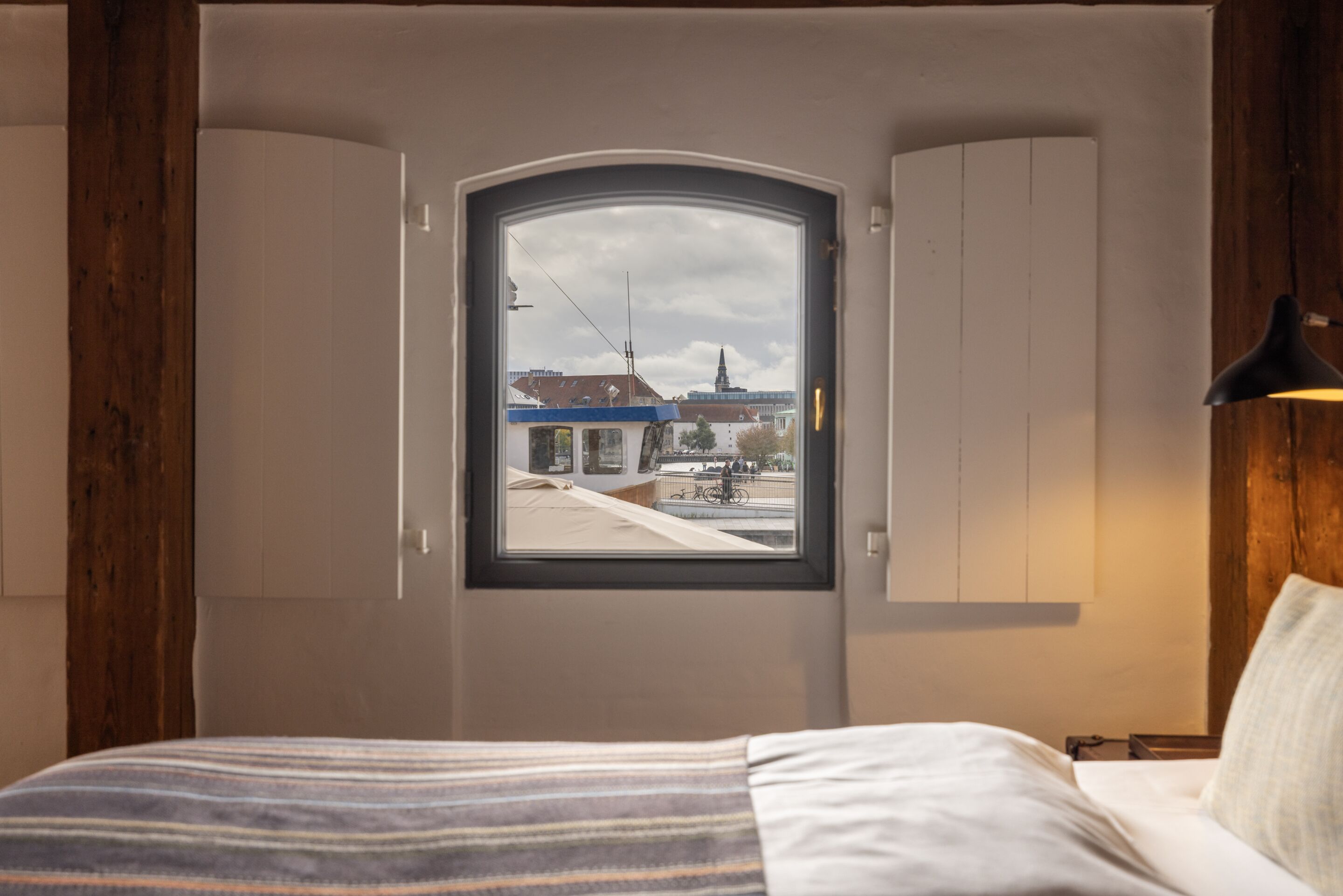 A bedroom with a large window, wooden beams, a bed, and a nightstand.