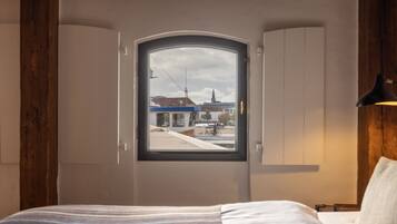 A bedroom with a large window, wooden beams, a bed, and a nightstand.