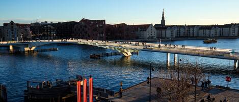 A riverside walkway with a bridge, buildings, and a boat dock.