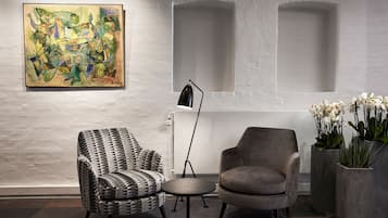Una habitación moderna con un sillón de estampado geométrico, una mesa redonda, una lámpara de pie y un cuadro en la pared.