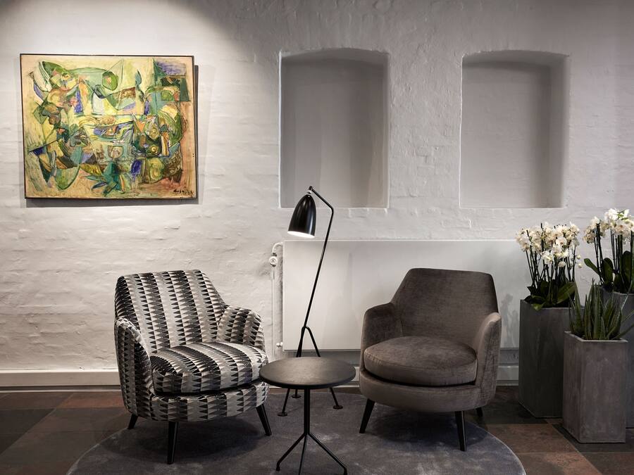 Une pièce moderne avec un fauteuil aux motifs géométriques, une table ronde, un lampadaire et un tableau accroché au mur.