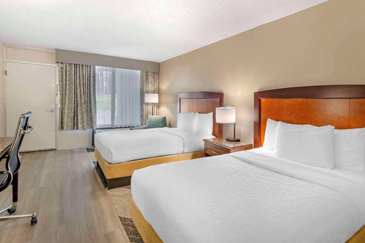 A hotel room with two beds, a desk, and a chair.
