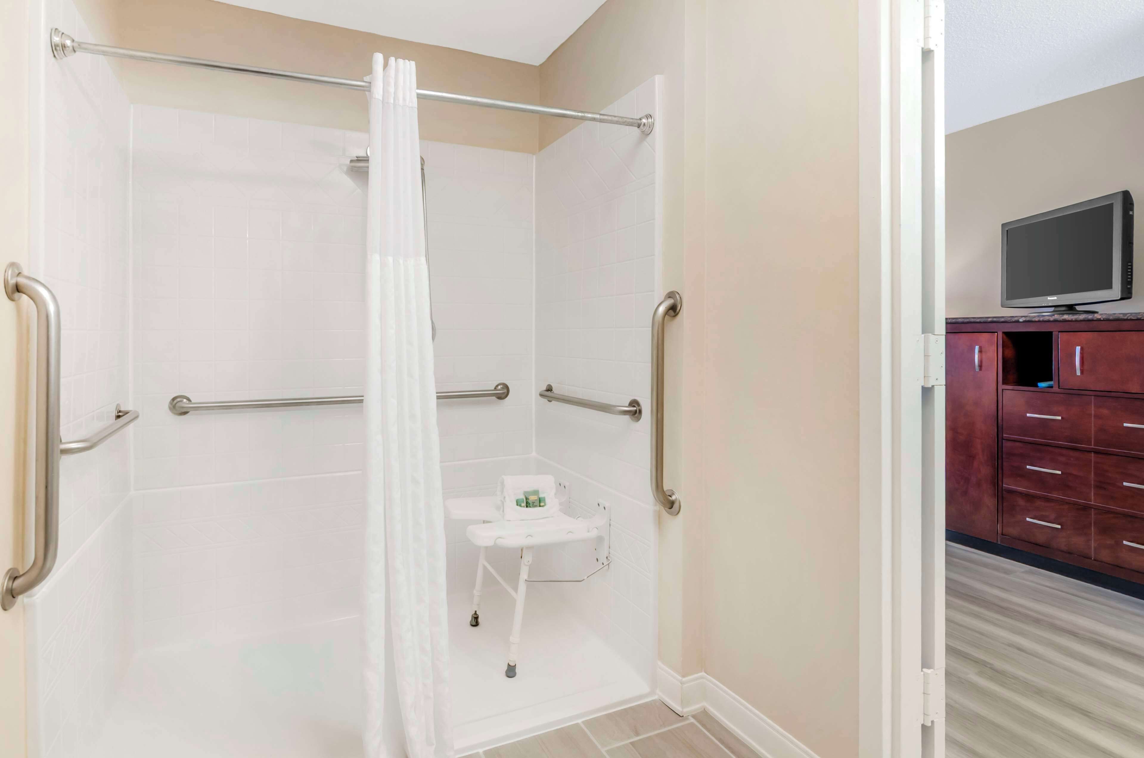Un baño con zona de ducha, barras de apoyo y un inodoro con asiento de seguridad.