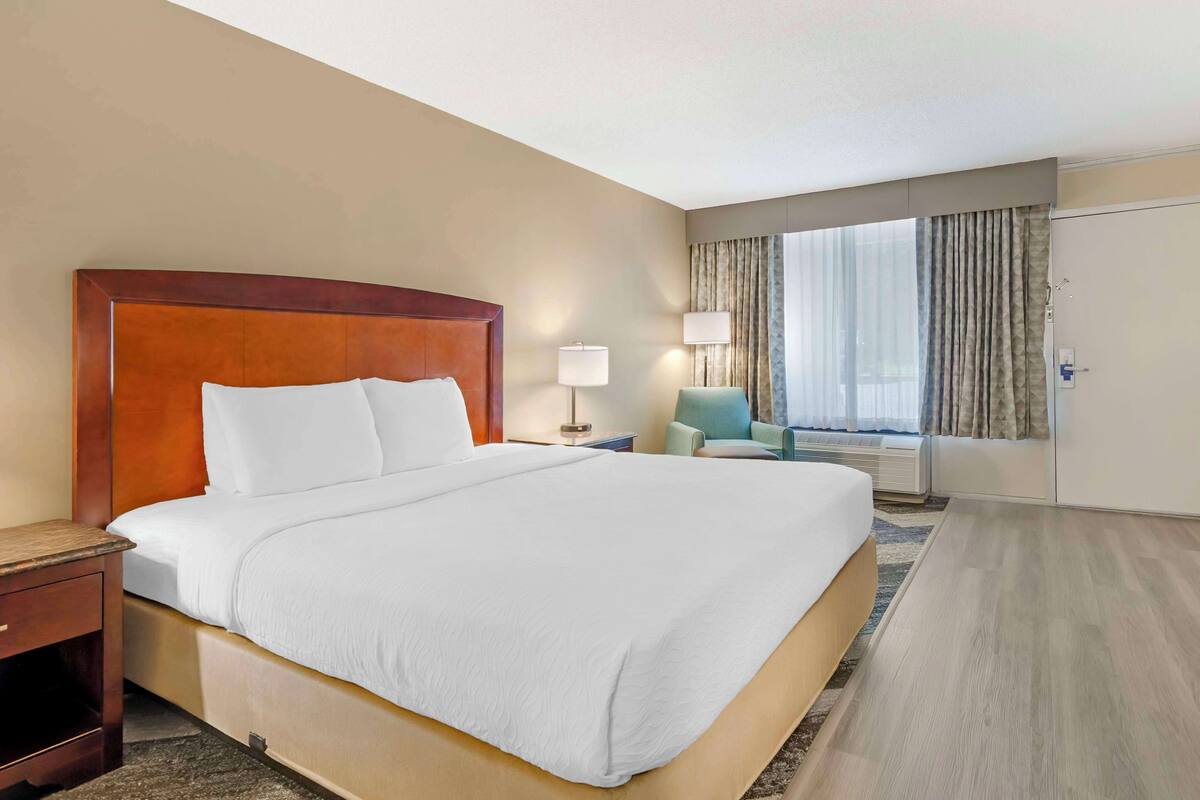 A hotel room with a large bed, bedside tables, a lamp, a chair, and a window with curtains.