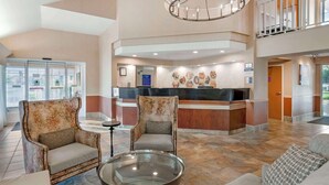 A spacious lobby with a reception desk, two armchairs, a glass coffee table, and a chandelier.