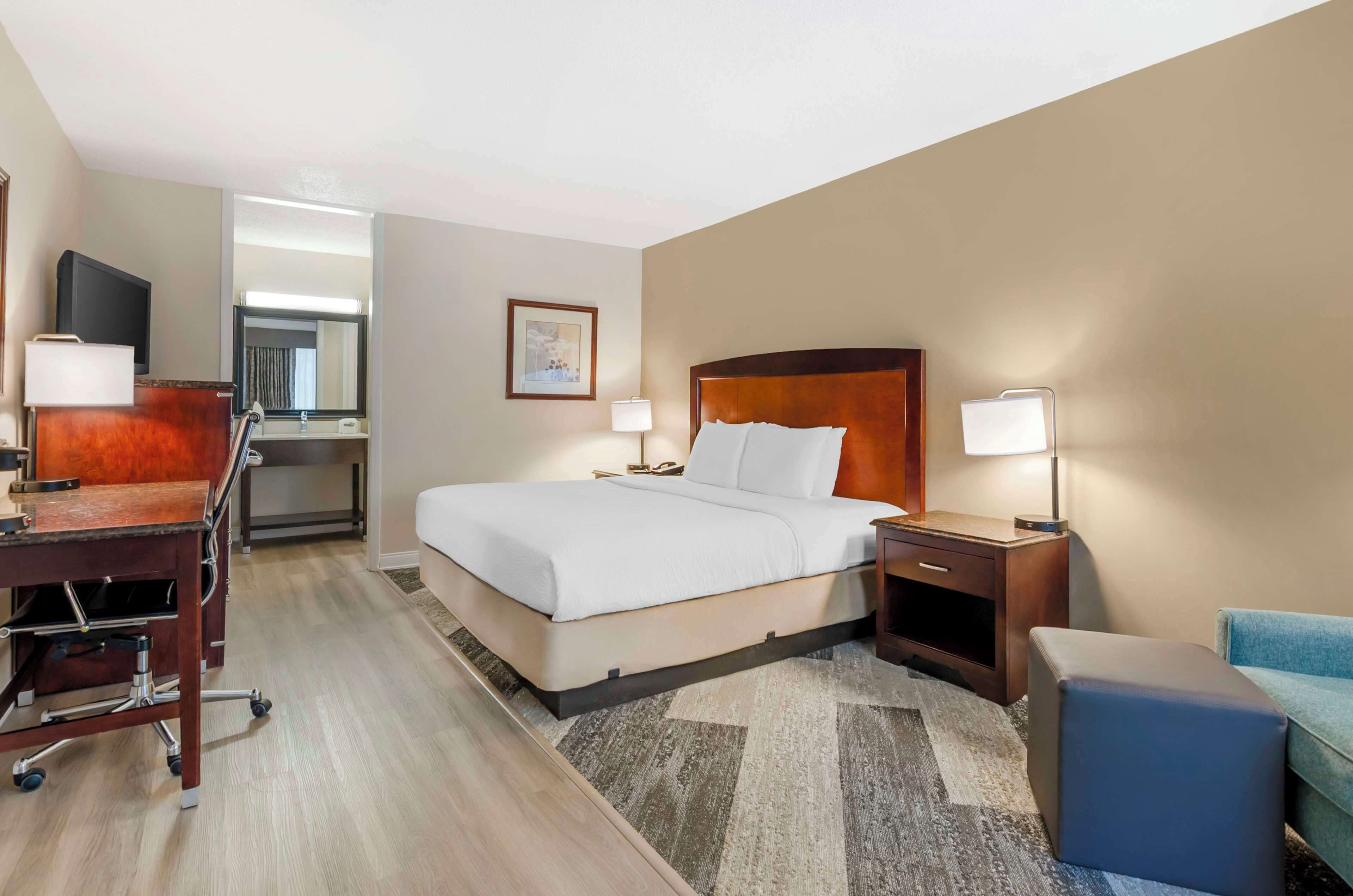 Quarto de hotel com cama, escrivaninha, cadeira e um pequeno espaço para sentar.