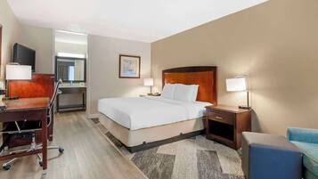 A hotel room with a bed, desk, chair, and a small seating area.
