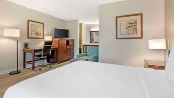 A hotel room with a large bed, a desk with a chair, a television, and two framed pictures on the walls.