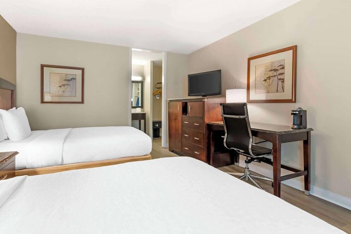 A hotel room with two beds, a desk with a chair, a television, and framed artwork on the walls.