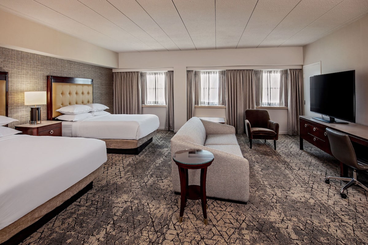 A hotel room with two beds, a sofa, a TV, a desk, and a small table.
