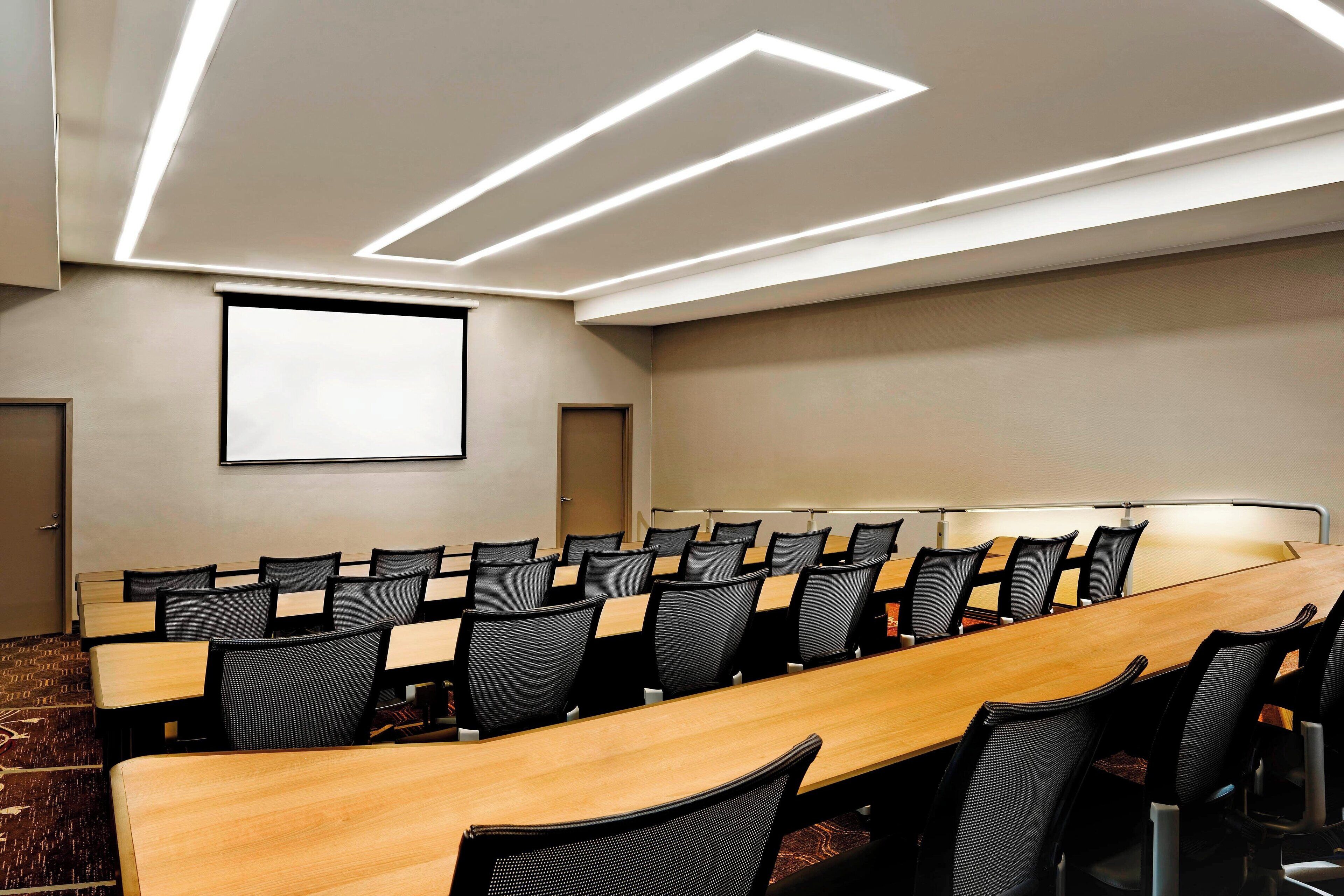 Une salle de conférence dotée d’une longue table, de nombreuses chaises, d’un écran de projection et d’un éclairage moderne.