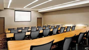 A conference room with a long table, multiple chairs, a projector screen, and modern lighting.