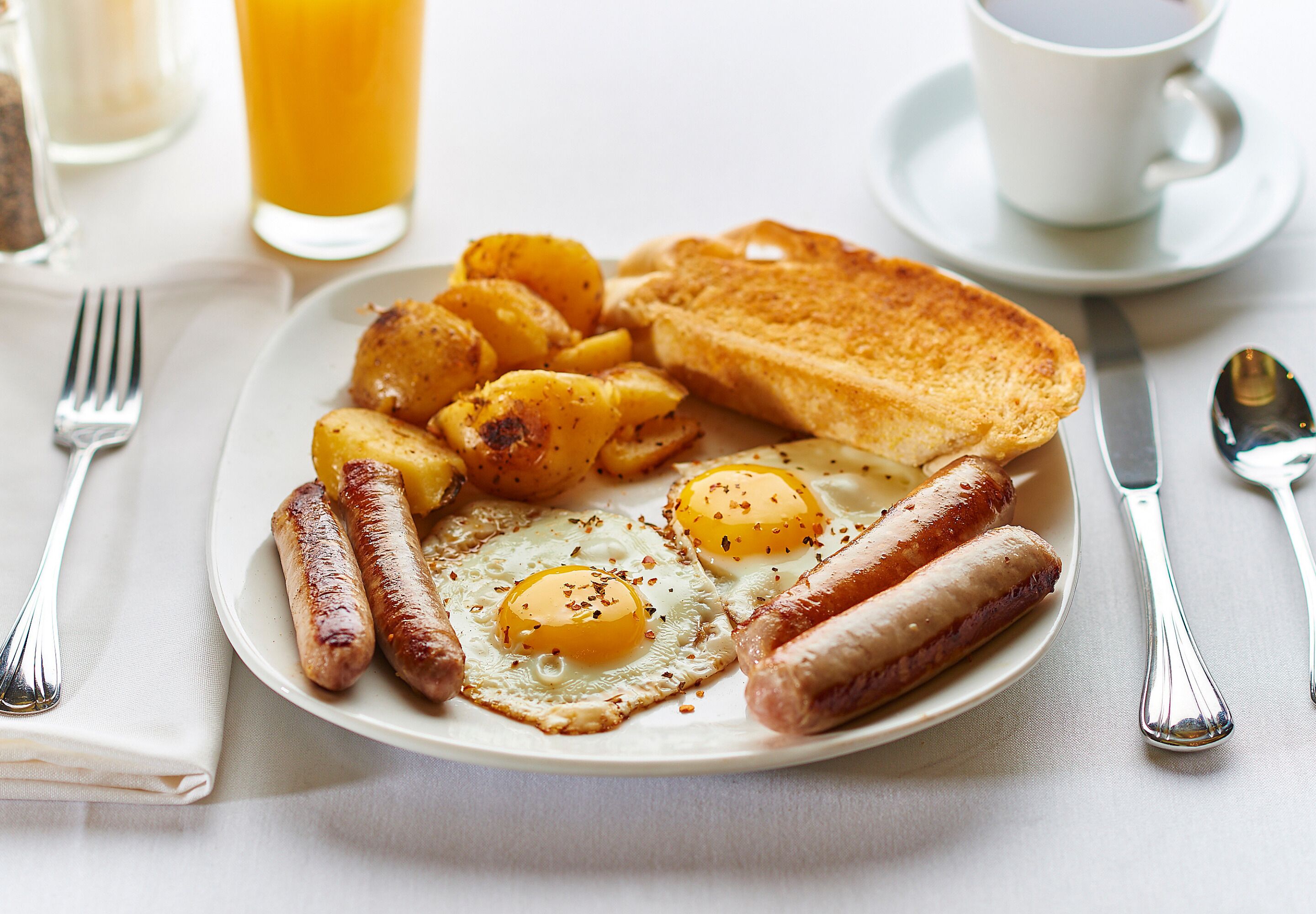 A plate of breakfast food including eggs, sausages, and toast, with a cup of coffee and a glass of orange juice on the side.