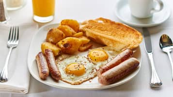 A plate of breakfast food including eggs, sausages, and toast, with a cup of coffee and a glass of orange juice on the side.