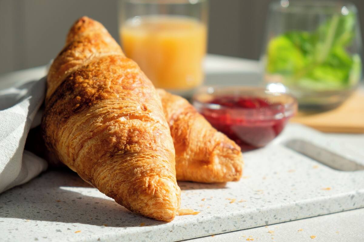 A croissant on a plate with a glass of orange juice and a bowl of jam.