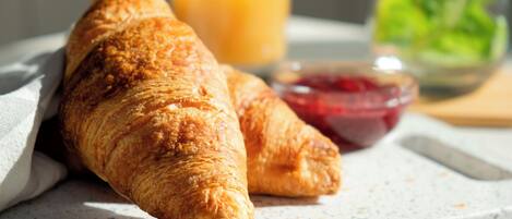 A croissant on a plate with a glass of orange juice and a bowl of jam.