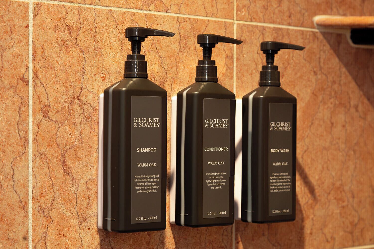 Tre prodotti Gilchrist & Soames: shampoo, balsamo e bagnoschiuma, ognuno etichettato con 'Warm Oak' e una capacità di 12,2 fl oz / 360 ml.