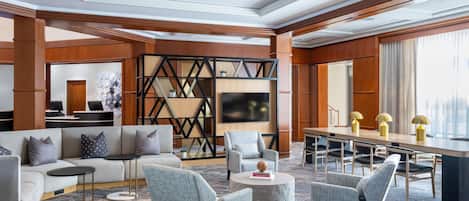 A modern hotel lobby with a seating area, a reception desk, and a large TV screen.