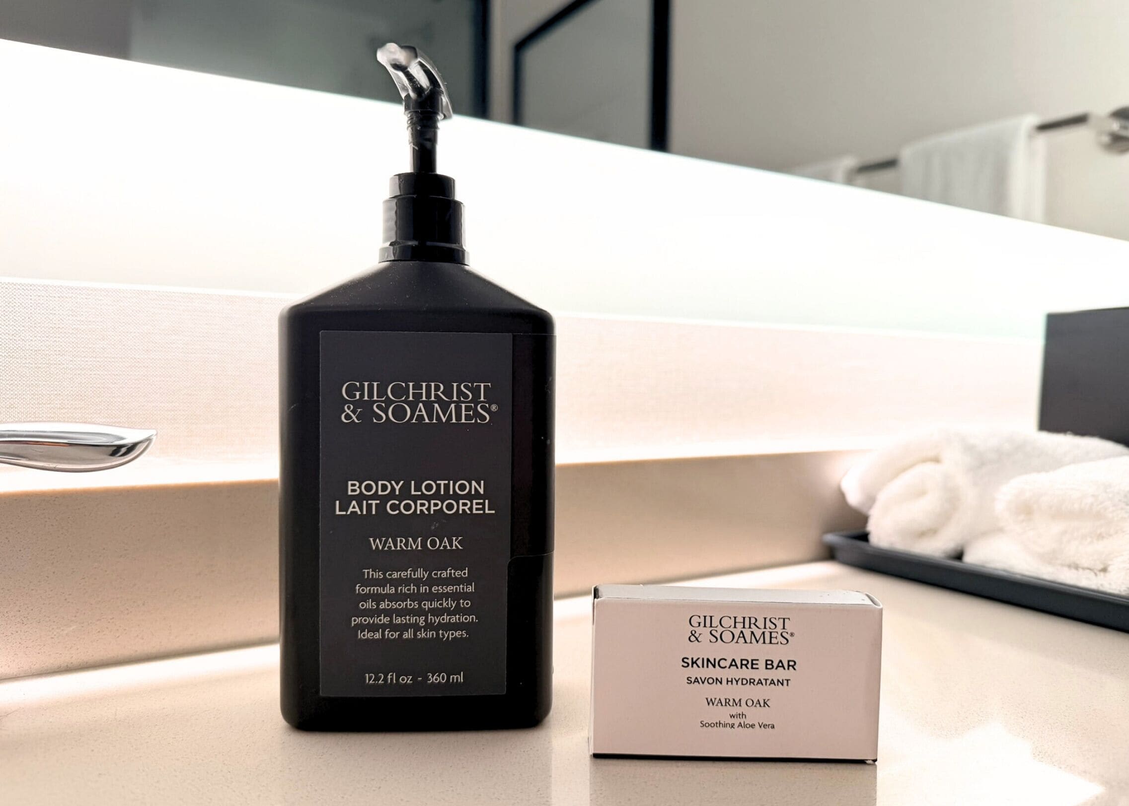 Un flacon de lotion pour le corps de la marque Gilchrist & Soames et un savon pour le visage sont posés sur le comptoir d’une salle de bain.