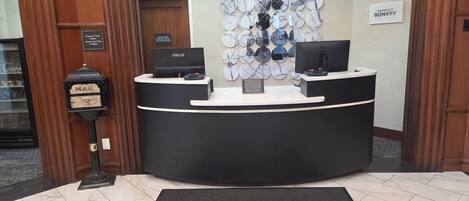Taulell de recepció d'hotel amb comptador d'entrada, un ordinador i una pantalla penjada a la paret.