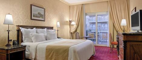 A hotel room with a large bed, two bedside tables, a dresser, a television, and a balcony with a railing.
