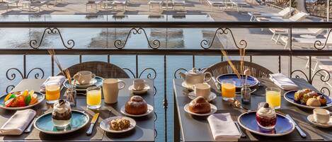 A terrace with tables set for breakfast overlooking the sea, featuring sun loungers and umbrellas.