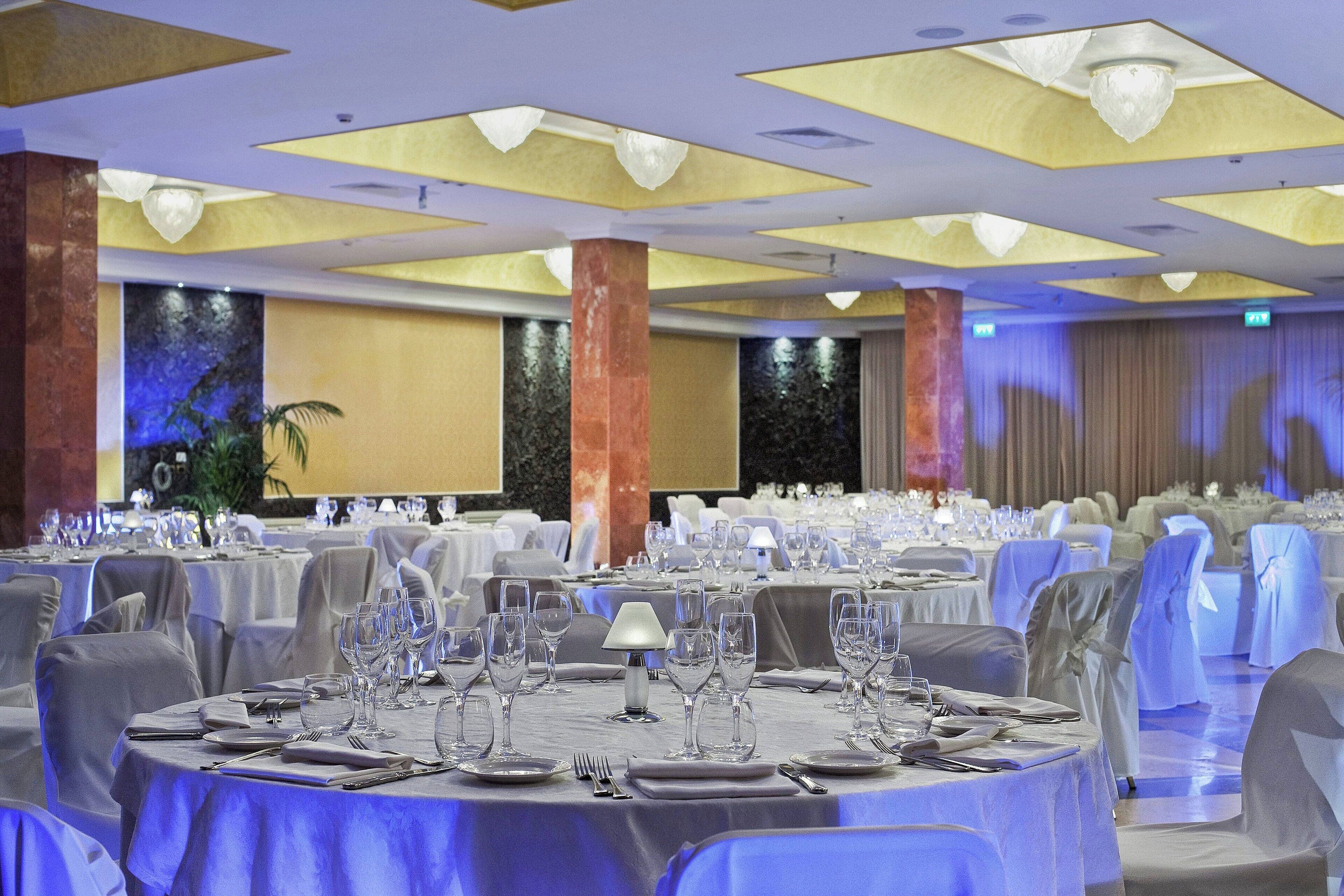 A banquet hall with round tables set for dining, featuring a ceiling with recessed lighting and a decorative waterfall wall.