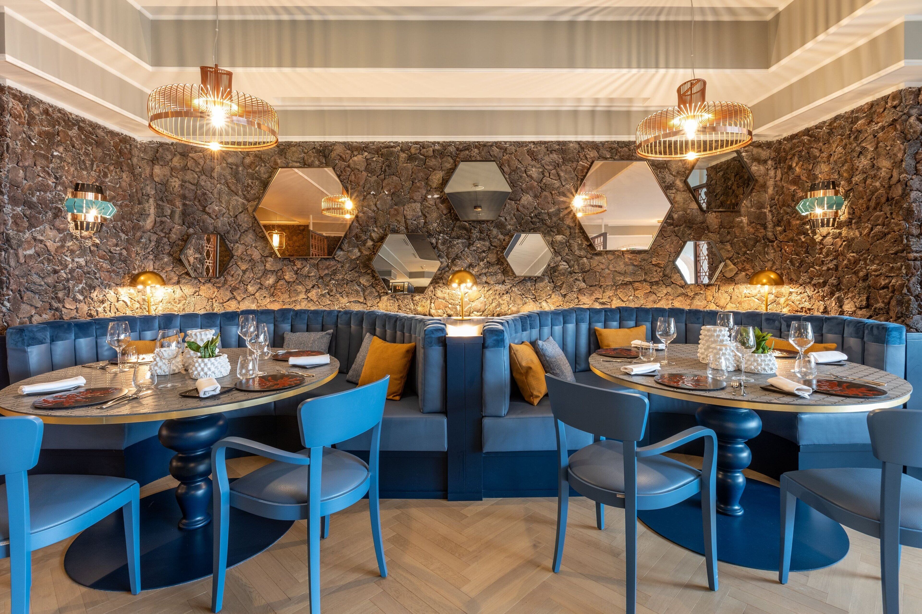 A restaurant with a stone wall, blue seating, and hexagonal mirrors.
