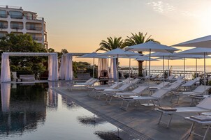 Zona junto a la piscina con sillones reclinables y sombrillas, una pérgola y vistas al mar.