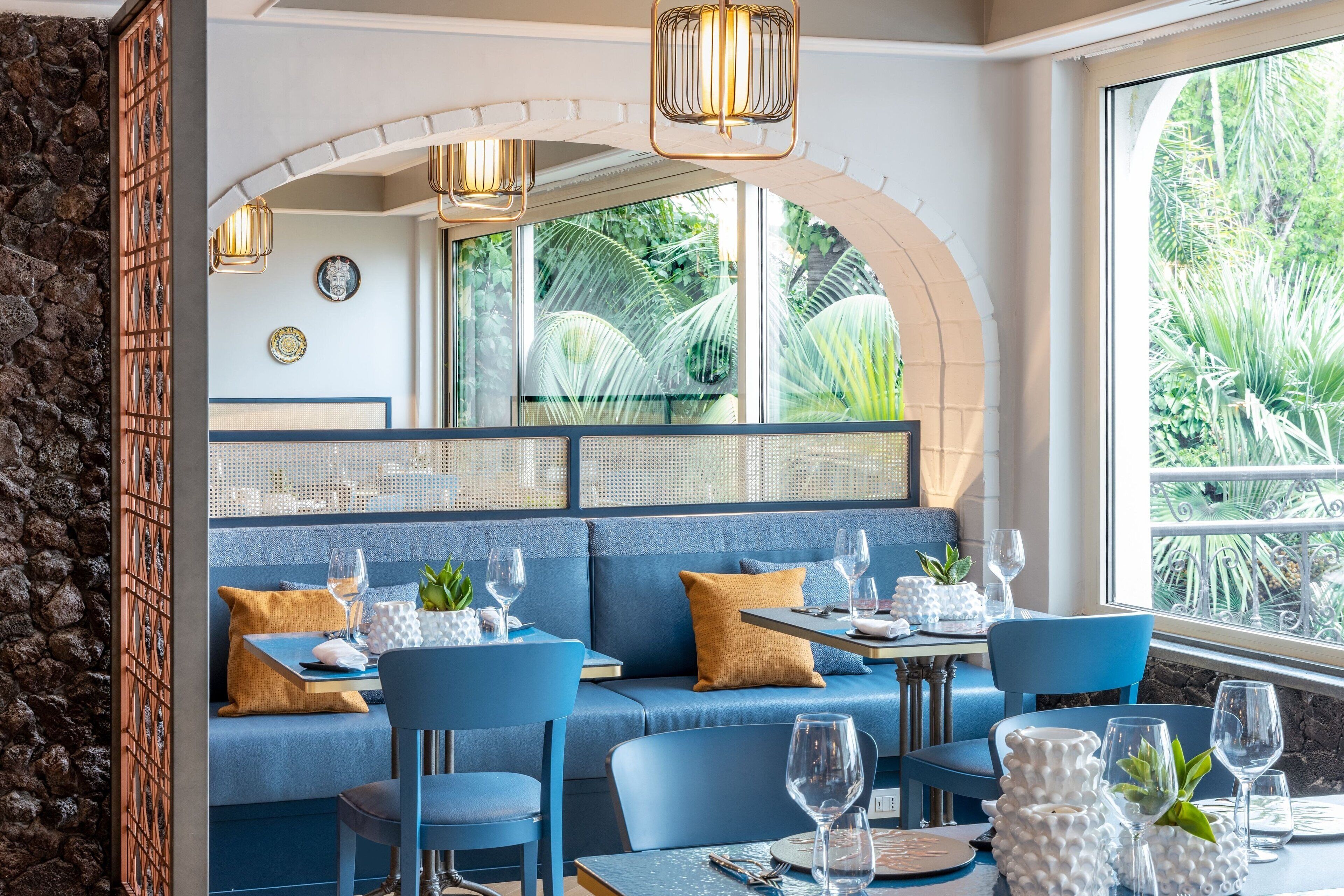 Ein Restaurant mit blauen Sitzgelegenheiten, einer Steinsäule und großen Fenstern mit Blick auf Grünflächen.