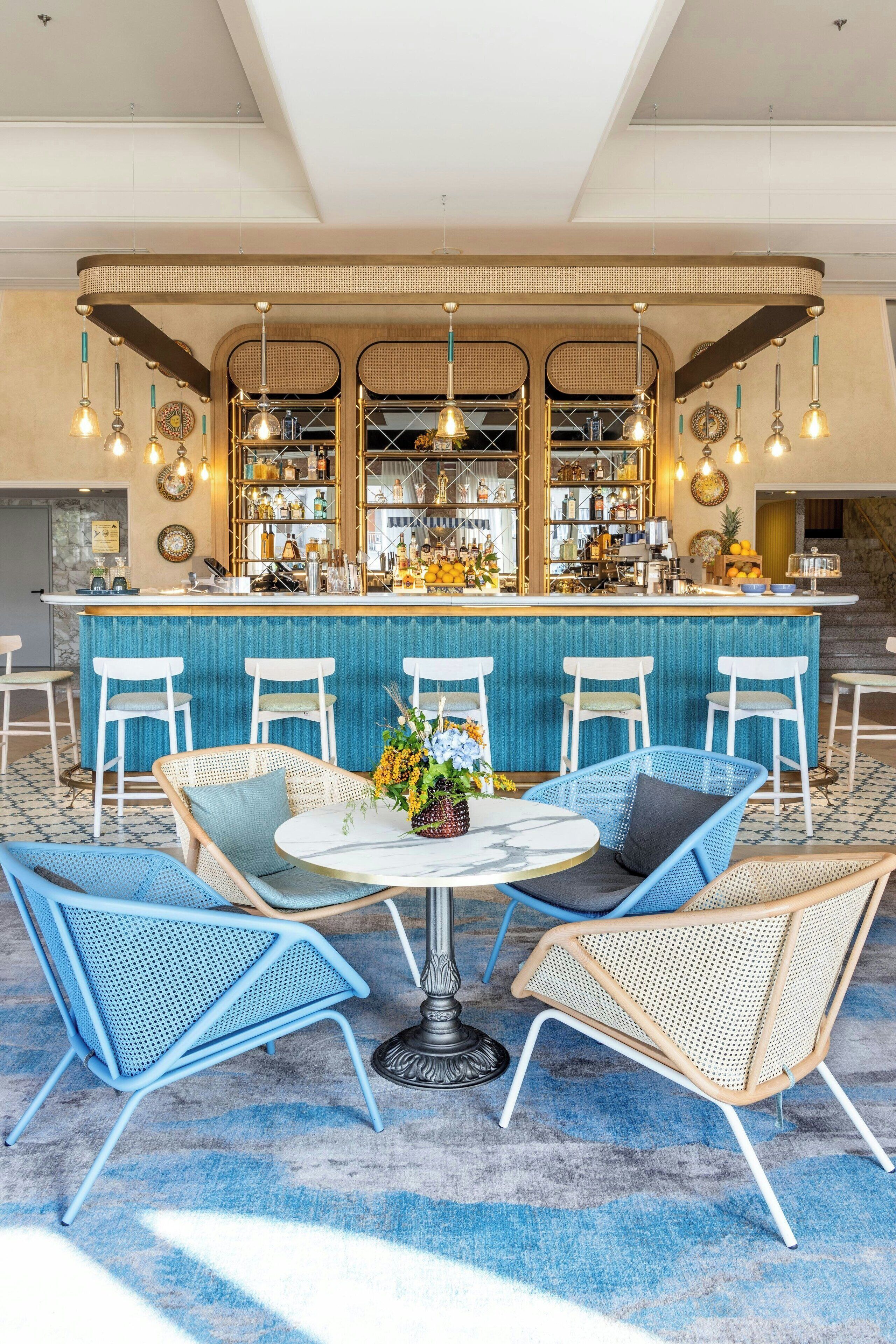 Una zona de bar con mostrador azul, sillas blancas y luces colgantes.