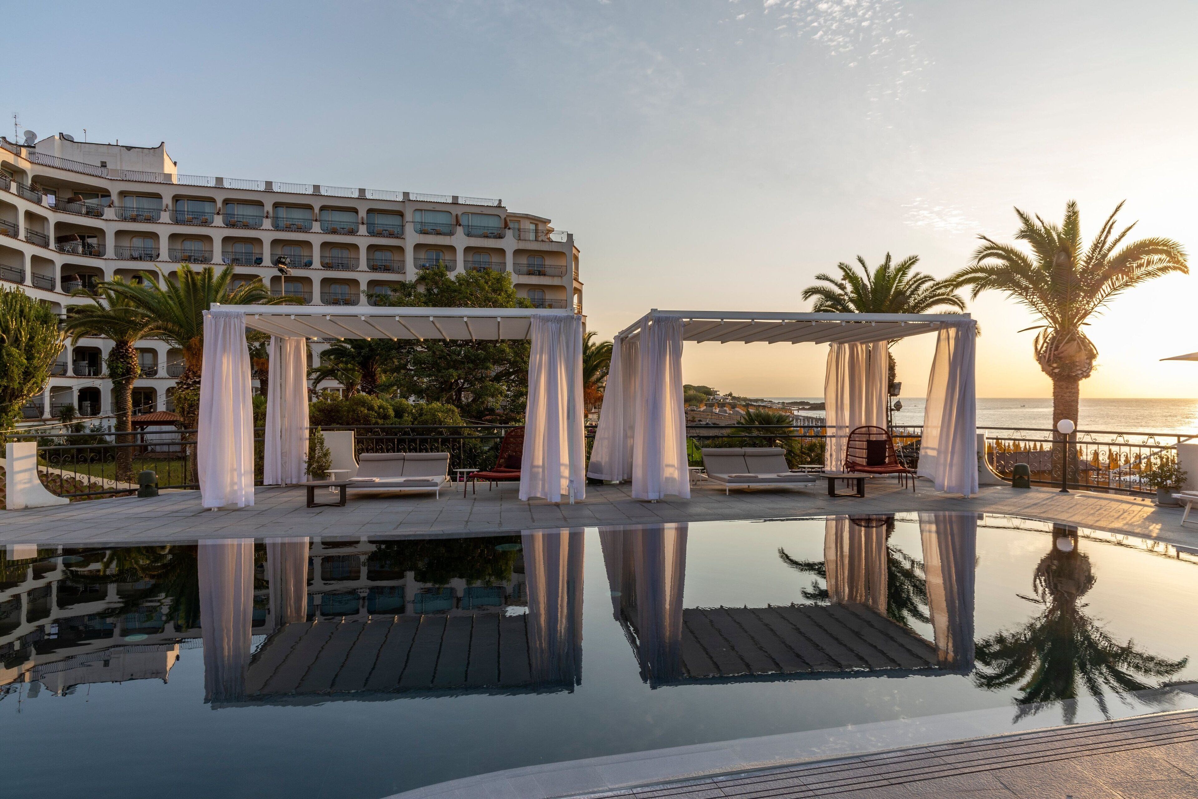 Un espace aménagé au bord de la piscine offrant une vue dégagée sur la mer, un grand bâtiment en arrière-plan et un kiosque.