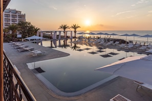 Ein Poolbereich mit Liegestühlen und Sonnenschirmen mit Blick auf ein Gewässer und einen Sonnenuntergang.